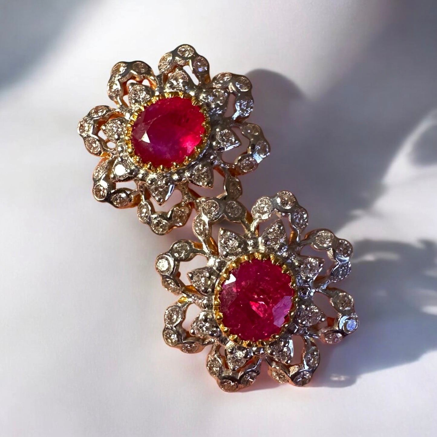 Pair of floral earrings with red gemstones and gold accents on a white background