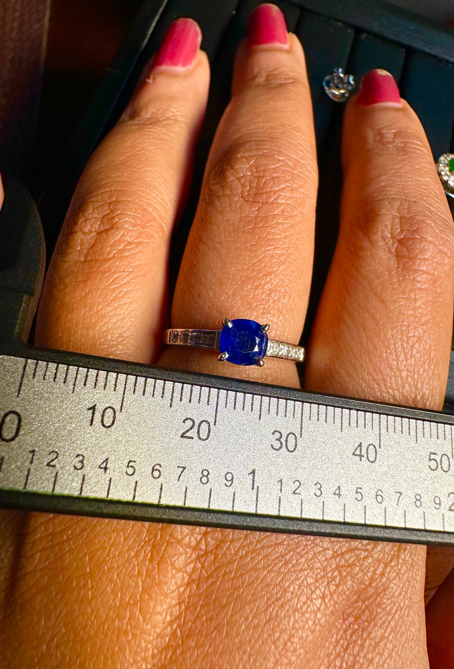 Close-up of a hand wearing a ring with a blue gemstone, held against a ruler.
