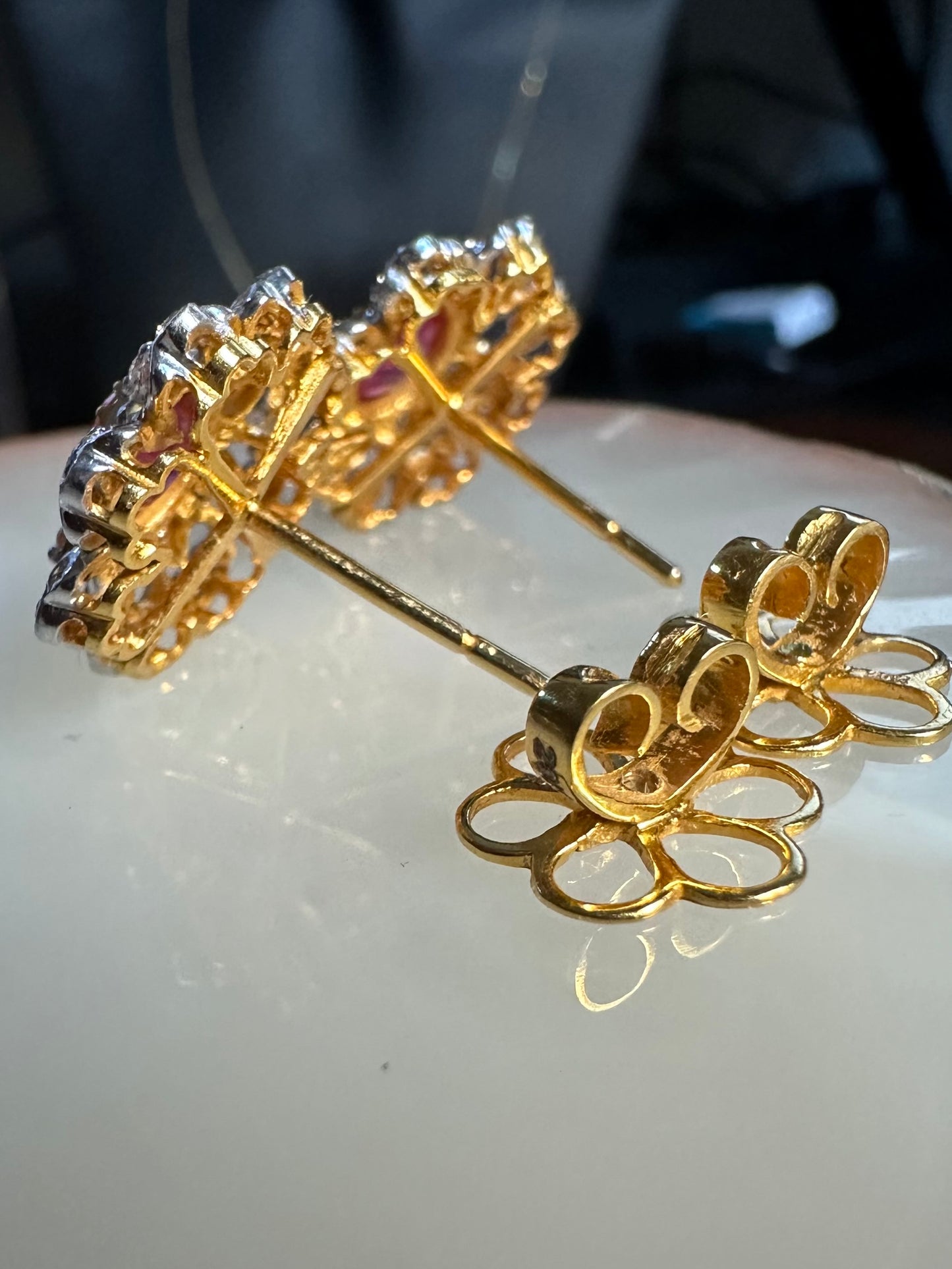 Gold earrings with intricate designs on a reflective surface