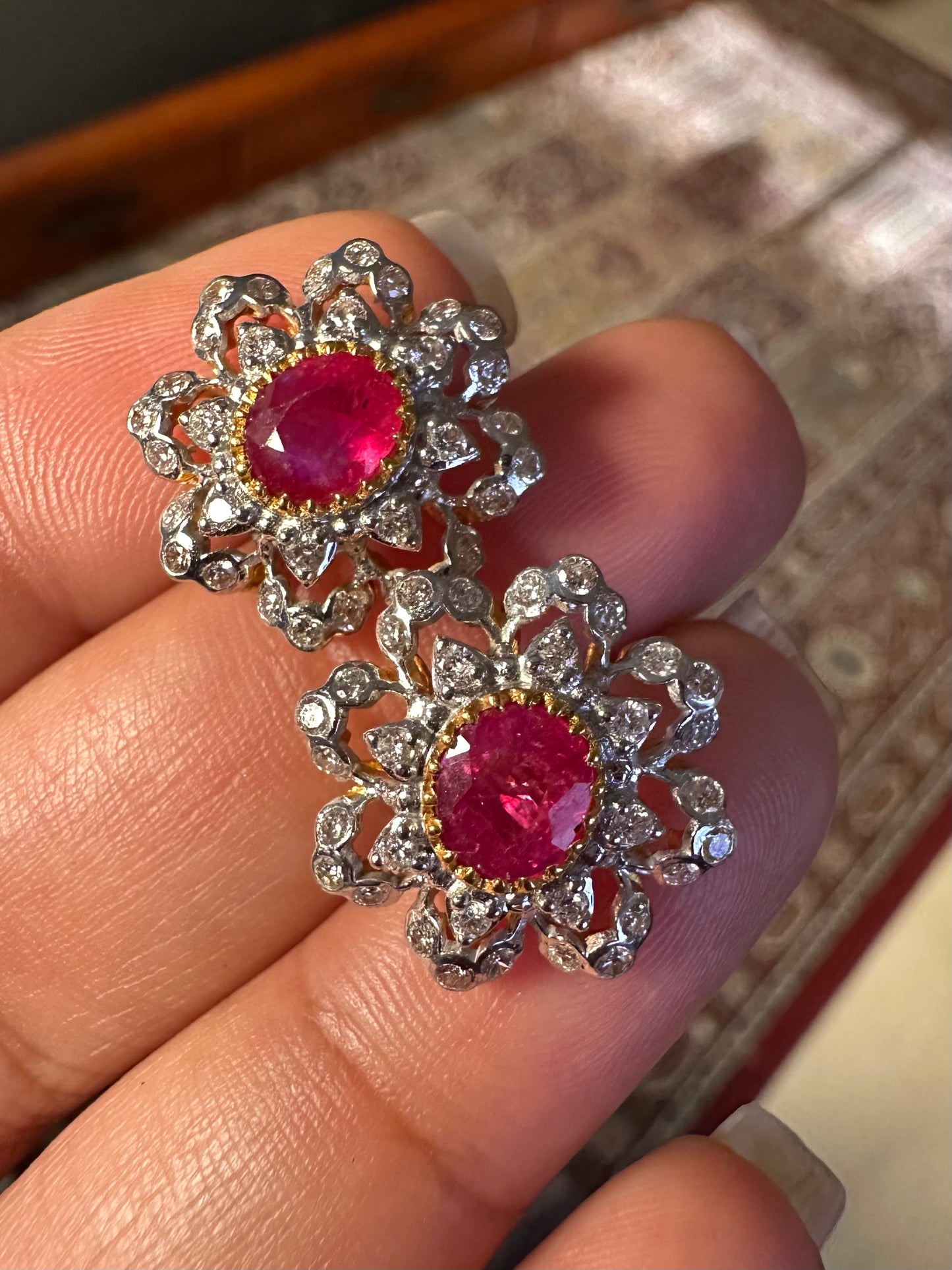 Pair of earrings with red gemstones and silver floral designs held by a hand.