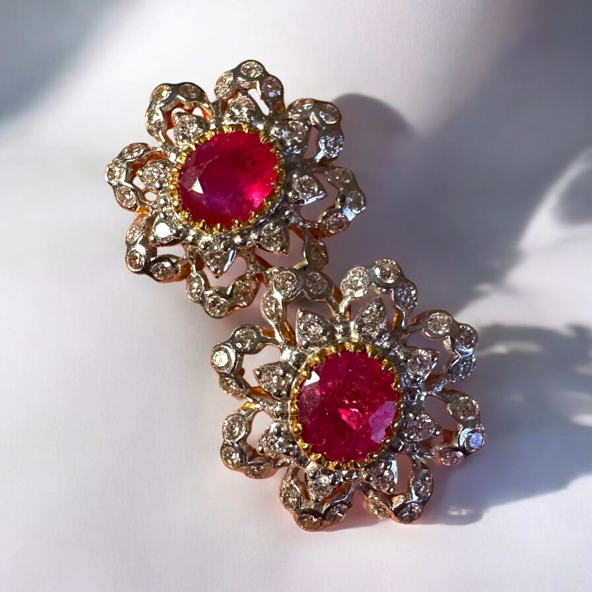 Pair of floral earrings with red gemstones and gold accents on a white background
