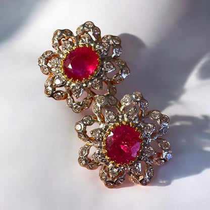 Pair of floral earrings with red gemstones and gold accents on a white background